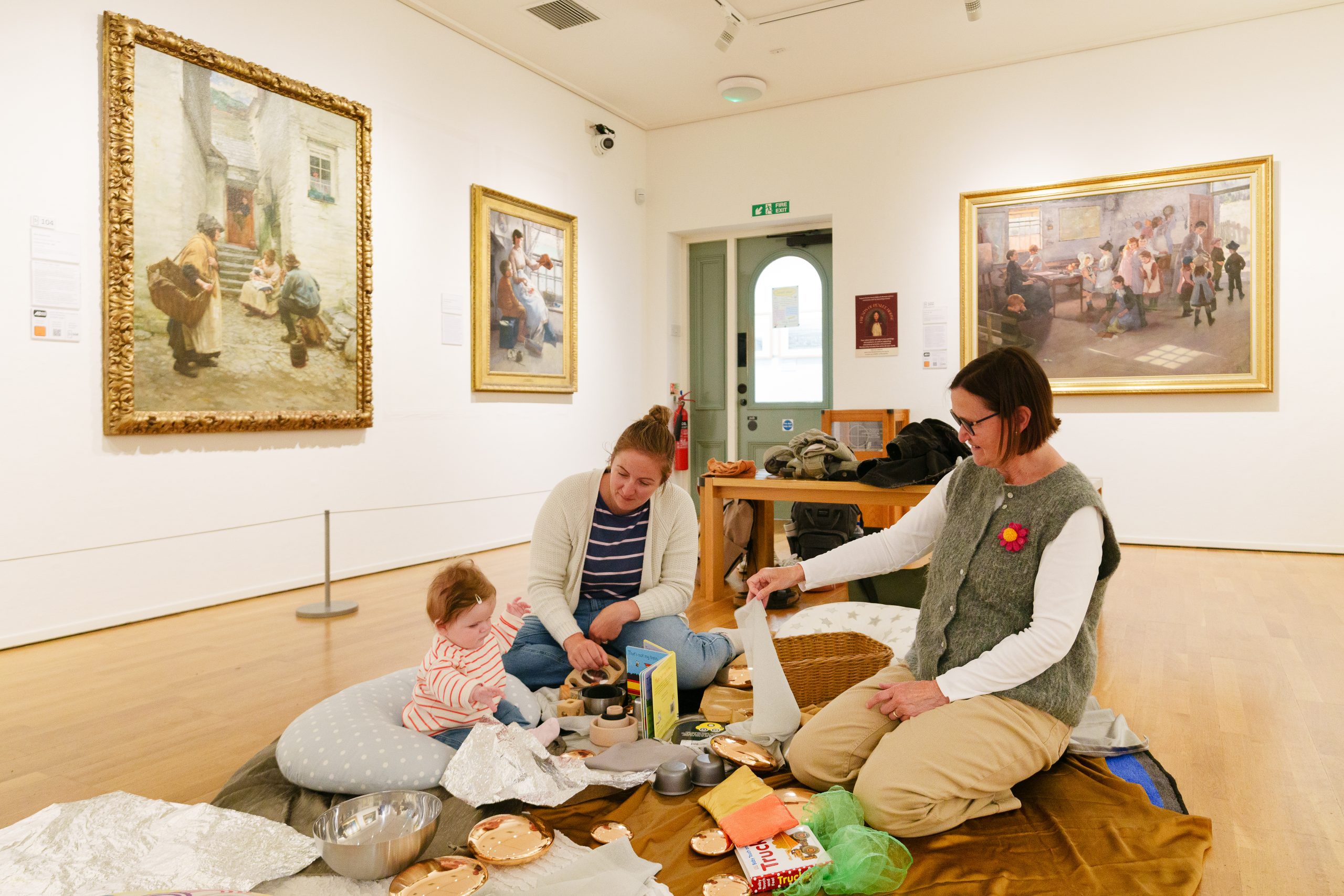 A family on the floor of an art gallery, surrounded by large framed paintings. The atmosphere is relaxed and informal.