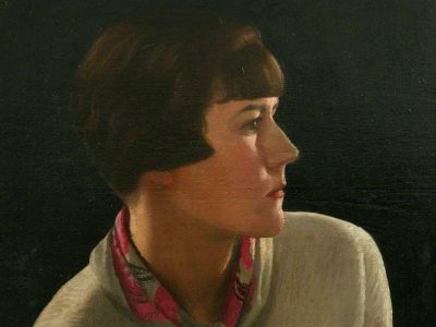 Portrait of a woman with short dark hair and a neutral expression, wearing a cream sweater and a red patterned scarf, set against a dark background.