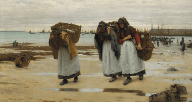 Three women in headscarves and white aprons walk across a sandy beach, carrying large woven baskets on their backs near a harbour with many boats.