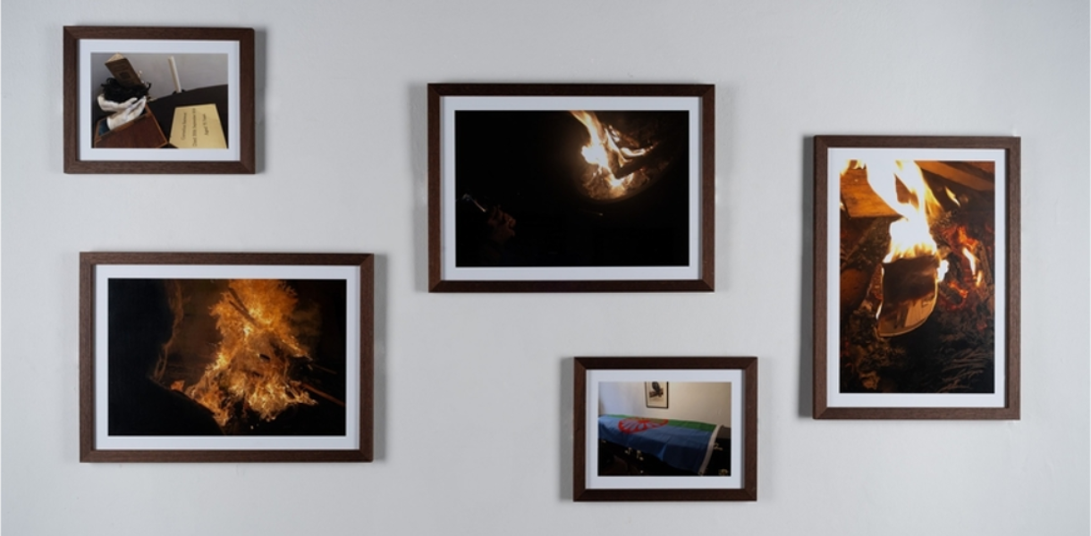 Five framed photographs on a grey wall show scenes of fire and everyday objects, creating a contrasting and dramatic visual display.
