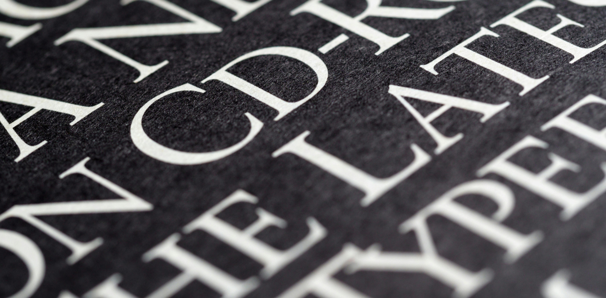 A close-up, angled view of white serif text printed on a textured black paper surface, with the words CD-R and LATE clearly visible in the foreground.